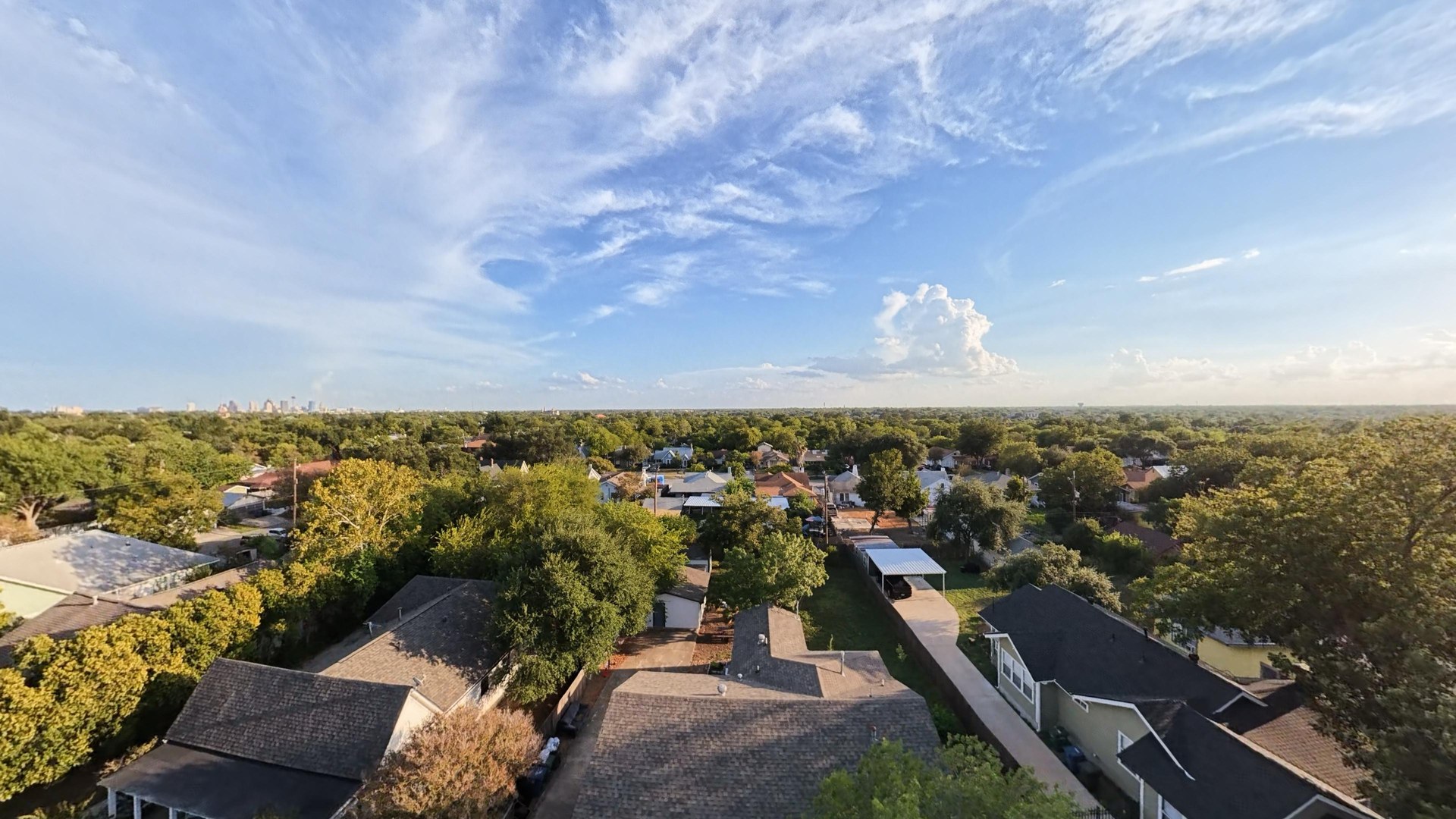 An aerial view across the Mulberry roof and surrounding trees toward the distant San Antonio skyline